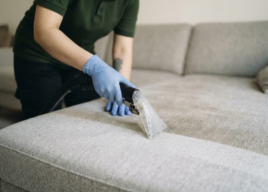 Mains gantées passant un injecteur-extracteur sur l'assise d'un canapé clair