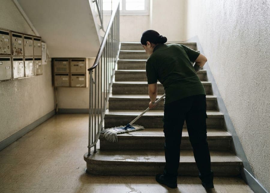 Intervenante passant la serpillère dans une cage d'escalier, boîtes aux lettres en fond